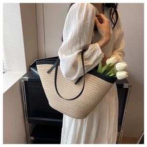 Detail of a beige woven straw tote bag with black trim and long leather shoulder straps