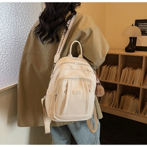 Vue de dos d'un sac à dos crème en similicuir avec bandoulière tissée et pompon dans un bureau