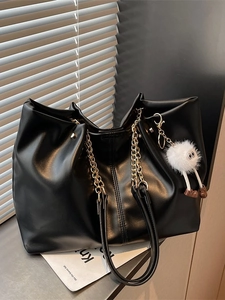 Fashionable black leather tote bag with gold chain strap and plush monster charm