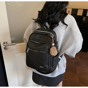 Detail of black pebbled leather backpack with silver zippers and a brown pom-pom charm