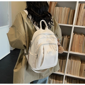 Détail du sac à dos blanc à motif litchi avec logo en lettres dorées et pompon en fourrure