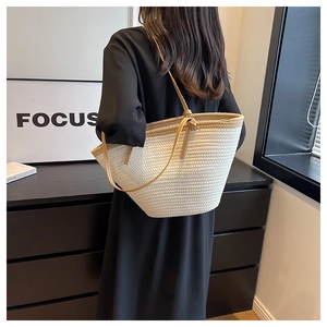 Detail of a white woven straw tote bag with brown leather straps worn by a model