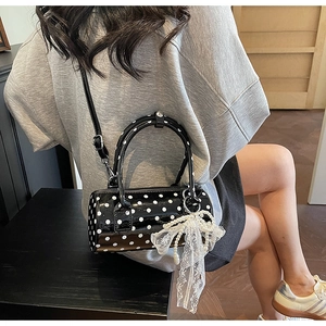 Close-up of a polka dot cylinder bag with glossy patent finish and lace pearl charm