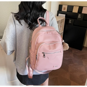 Close-up of pink faux leather backpack with litchi texture and plush ball charm detail