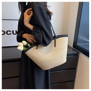 Close-up of woven straw tote bag featuring black leather handles and texture detail