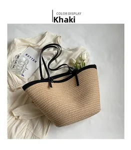 Close-up of khaki woven straw tote bag with black leather straps on a white fabric background