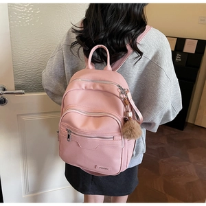 Detail of pink faux leather backpack with pom-pom charm and sleek zipper pocket