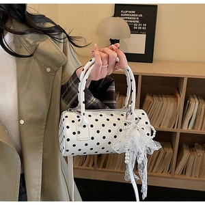 Close-up of a polka dot Boston bag with lace bow and pearl chain detail in a lifestyle setting