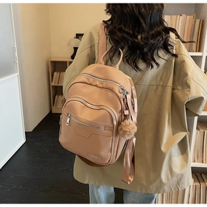 Detail of khaki faux leather backpack with side brown fur pompom ball accessory
