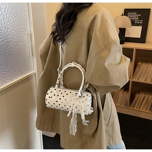 Close-up of polka dot cylinder bag with lace bow and pearl tassel on a beige coat