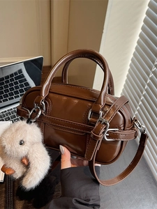 Chic dark brown faux leather Boston bag with plush pendant in an office setting