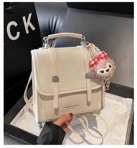 Detail of cream leather handbag with adjustable straps and plush bear keychain decor