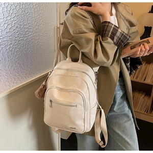 Detail of cream white faux leather backpack with multiple zipper pockets and plush ball