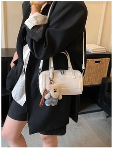 Detail of white leather shoulder bag with a cute teddy bear charm on a bookshelf background