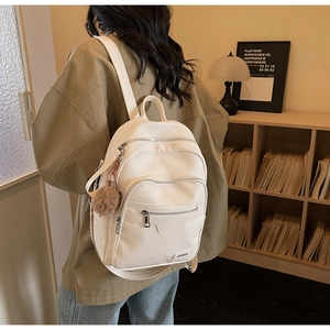 Detail of white litchi pattern PU leather backpack with multi-zipper and fur ball charm