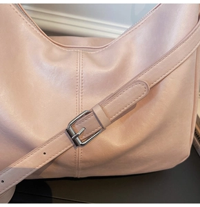 Detail of light pink shoulder bag showing smooth synthetic leather and silver metal buckle