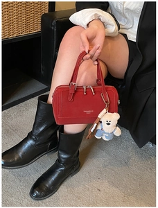 Detail of a red Boston handbag with dual handles and a cute bear plush charm accessory