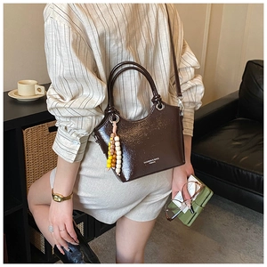 Vue détaillée du sac seau marron brillant avec breloque perlée et lettrage chic