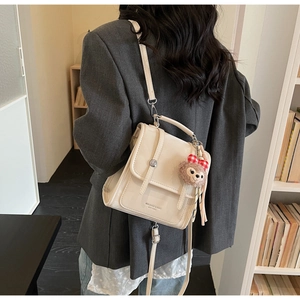 Detail view of cream vintage satchel bag worn by model with a cute plush bear pendant