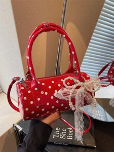 Red polka dot Boston bag with pearl bow detail and glossy finish on a retro desk