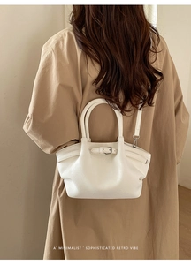 Detalle de un bolso tipo cubo blanco roto minimalista con textura de cuero y hebilla retro