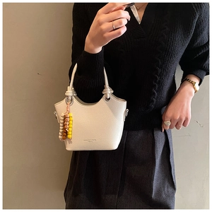 Detail der cremefarbenen Ledertasche mit Knotengriff und Perlenanhänger-Accessoire