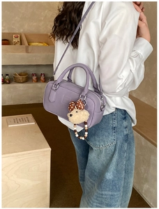 Détail du sac bowling en cuir violet avec breloque ours porté par un mannequin