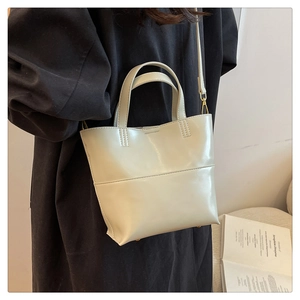 Vue latérale du sac cabas en cuir beige avec boucles dorées porté par un mannequin