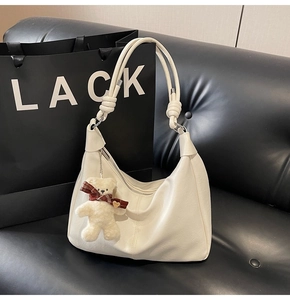 Detail of cream white faux leather hobo bag with knotted strap and teddy bear charm