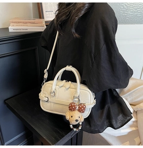 Detail of cream white handbag featuring a teddy bear charm and removable shoulder strap