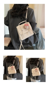 Detail of cream messenger bag with metal buckle and plush bear charm decoration