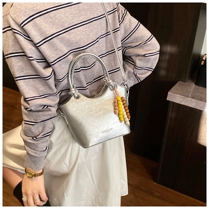 Detail einer silbernen Metallic-Eimertasche mit Perlenanhänger und feinem Schultergurt