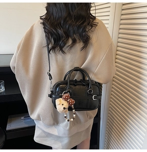 Detail view of black handbag with textured leather, dual zippers and cute bear charm