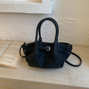 Detalle de bolso tipo cubo negro mate con hebilla plateada sobre fondo de mármol