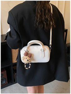Vue détaillée du sac boîte en cuir blanc avec breloque ours sur blazer noir chic