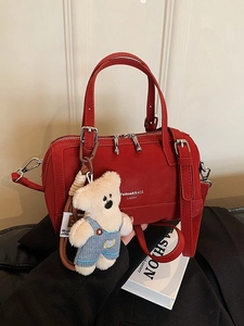 Elegant red leather Boston handbag with top handles and a cute white teddy bear charm