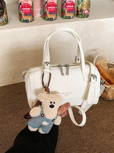 Chic white leather handbag with double zippers and cute brown bear charm on vintage background
