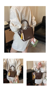 Detail einer glänzenden braunen Beuteltasche mit Goldringgriffen und bunten Perlenanhängern