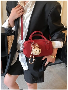 Détail d'un sac bowling rouge avec breloque ours en peluche porté sur un blazer noir