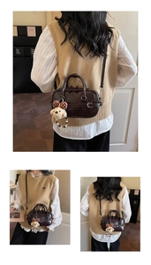 Detail view of deep brown faux leather handbag with buckle strap and plush bear charm