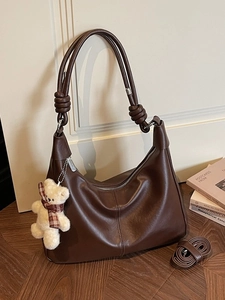 Deep brown leather hobo bag with a plush bear charm and adjustable shoulder strap