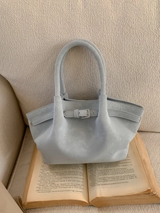 Bolso cubo azul claro con hebilla decorativa sobre libro antiguo y sofá beige