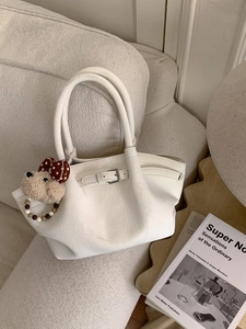 Bolso saco de cuero plisado blanco con colgante de cachorro de peluche en un sofá crema