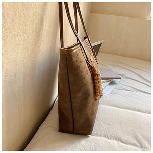 Detail of dark brown tote bag featuring embossed heart patterns and beaded charm accessory