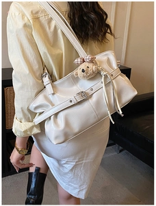 Detail of a beige tote bag with buckle straps and a cute plush bear pendant on a model