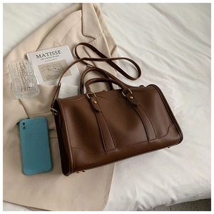 Brown leather Boston bag detail with gold hardware on a bed with lifestyle props