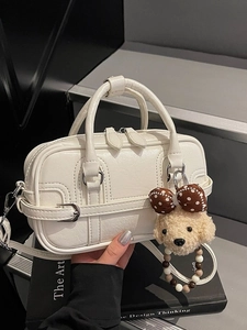 White faux leather top handle crossbody bag with plush poodle charm on design books