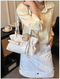 Detailed view of cream patent leather tote with buckle strap and brown plush bear charm