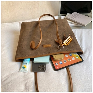 Detail of dark brown tote bag with leather embossing, holding a tablet and phone