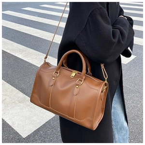 Brown leather Boston bag with gold zippers worn as a shoulder bag on street backdrops